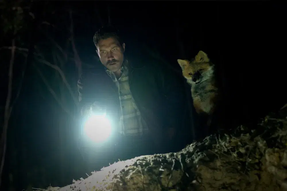 A mustached Jai Courtney and an lifelike puppet fox peer by the light of a flashlight into an unseen pit of horrors in Aussie film The Fox.