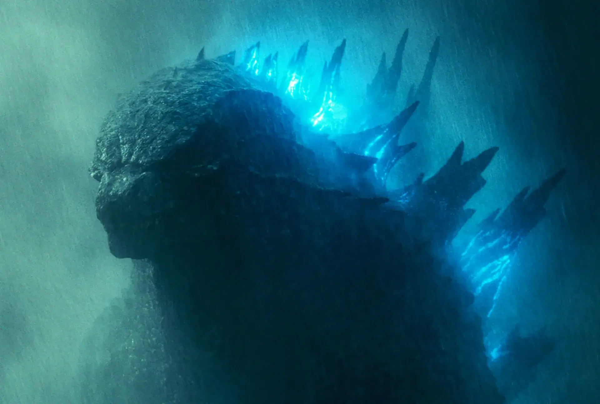 Legendary’s Godzilla in profile, backlit and mostly in silhouette in the rain, with glowing blue dorsal plates along his back.
