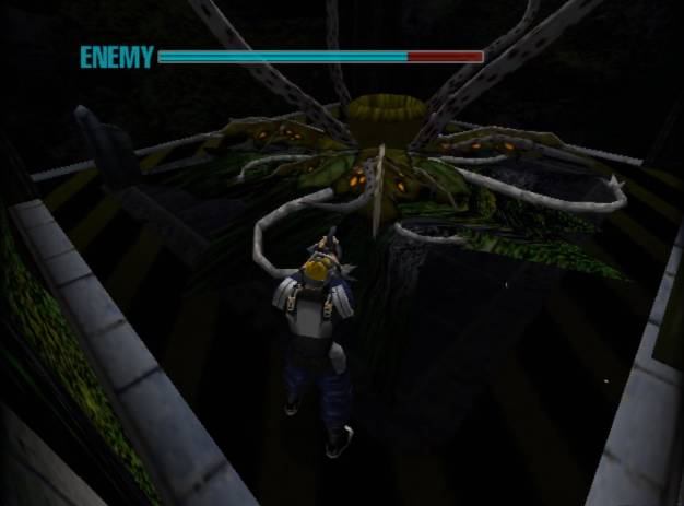 A low-resolution 3D screenshot from a video game, depicting a boss battle. The player character, seen from behind, is suspended in the air, possibly falling or hanging, wearing a blue and grey suit with a backpack and a yellow helmet. They are aiming a weapon upwards towards a massive, grotesque spider-like creature with a yellow-green body, multiple glowing orange eyes, and several thick, segmented legs that extend into the dark background. The creature is positioned above a dark, cavernous abyss, with industrial-looking structures visible on the left and right edges of the screen, suggesting a precarious environment. At the top of the screen, a red "ENEMY" health bar is visible with a blue overlay, indicating the creature is taking damage.