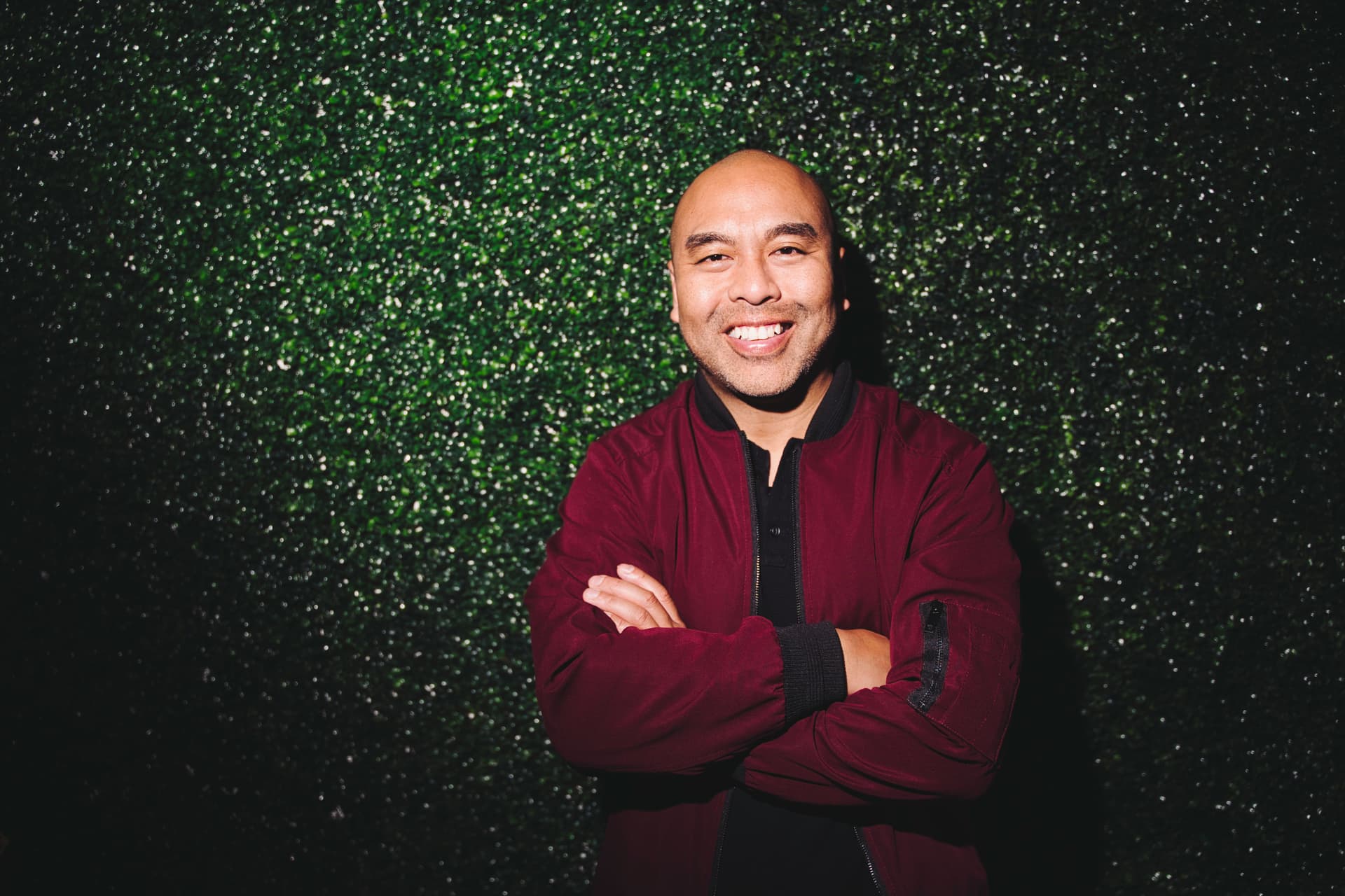 Jet Bunditwong, Asian Podcast host, standing against ivy walls, smiling with his arms crossed